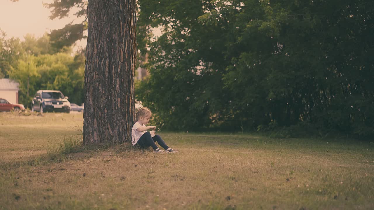young girl eats yogurt with large spoon sitting at tree