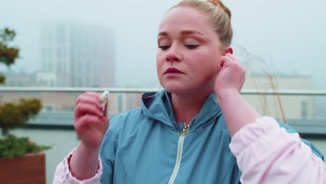 Sport-fitness-woman-wears-wireless-earphones-in-start-of-her-workout-training-on-roof-of-house