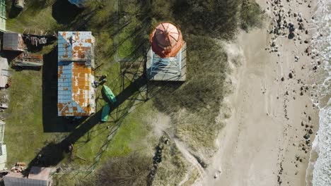 aerial establishing view of white colored pape lighthouse, baltic sea coastline, latvia, white sand beach, large waves crashing, sunny day with clouds, wide birdseye drone shot moving forward