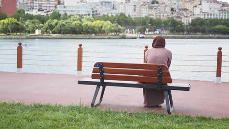 mujer sentada en un banco junto al río en un parque de la ciudad