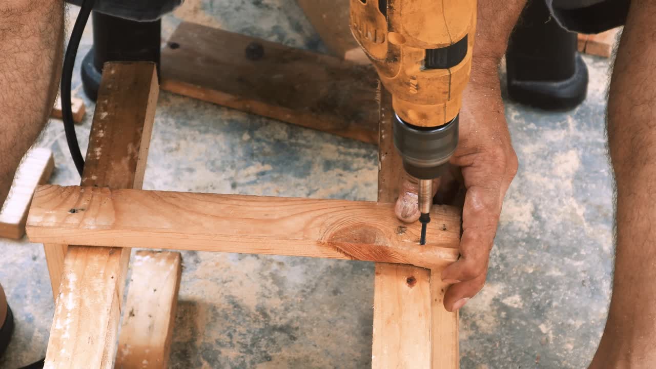 carpintero hábil que emplea un taladro eléctrico para colocar tornillos en una pequeña silla de madera en su pequeño taller para vender y apoyar la economía local