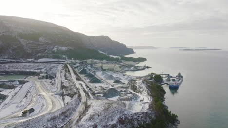 cargo ship docked at aggregate quarry with open pit stockpile, aerial