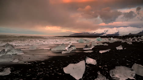 Olas-Salpicando-Trozos-De-Hielo-Varado-En-La-Orilla-De-Arena-Negra