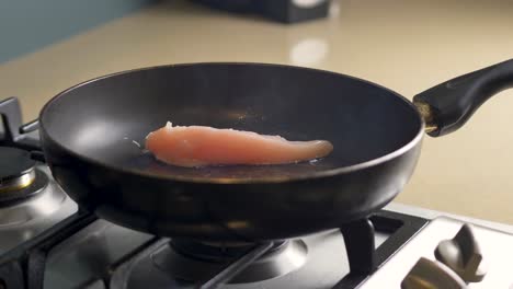 close-up slow motion shot of raw chicken placed on grill fry pan cooking on gas stove top bench oil and smoke heat kitchen restaurant food 4k