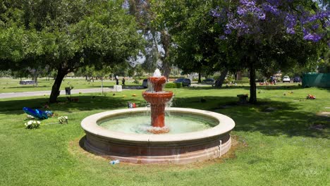 low panning aerial shot of a decorative fountain surrounded by flowered grave sites at a mortuary in california