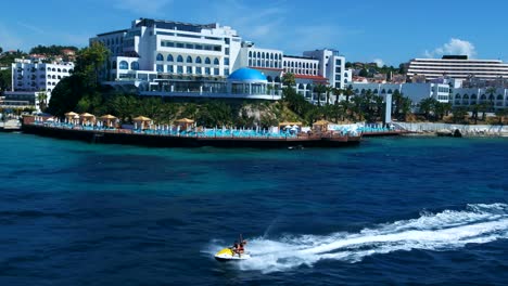 una pareja está montando un jetski en el mar con hoteles de lujo en el fondo