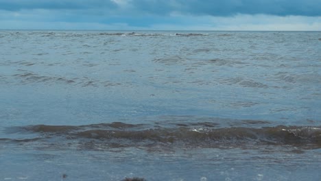 ocean sea water splattering to beach sand with white water and bubble in slow motion during a windy summer cloudy day in saaremaa estonia at a place called mändjala beach