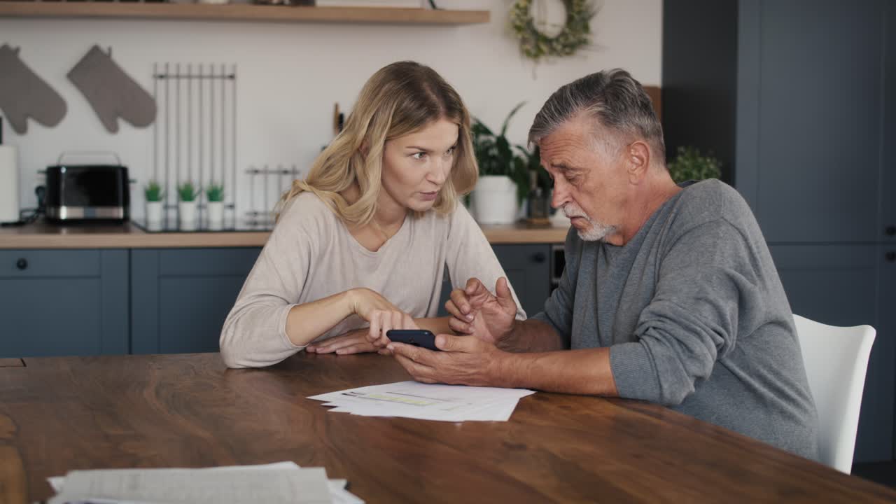 Kaukasisk kvinne som hjelper eldre mann med å bruke mobiltelefon