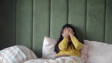 little girl hiding her face while lying in bed