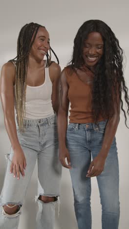 studio beauty portrait shot of two young women laughing and talking as camera rotates 2