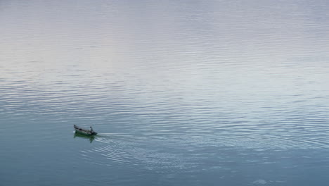 Wooden-boat-floating-still-river-drone-shot.-Calm-waterway-ripples-surface.