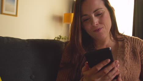 laughing woman sitting on sofa at home using mobile phone to check social media message and scrolling online 5