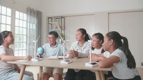 asian group of thoughtful kids study about ecology problems and their solution with wind turbine model and globe at school. renewable energy
