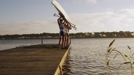 equipo de remadores masculinos llevando el bote por encima de su cabeza