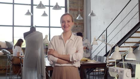 blond woman looking at camera in a tailor shop, in the background a colleague sitting at a table