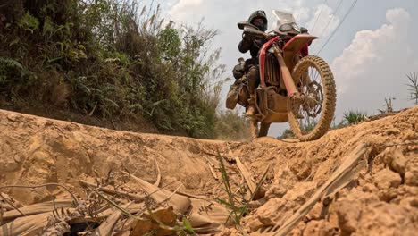 dry hillside terrain with rocky path winding through sparse trees and golden ground cover, low angle view of motorcycle rider