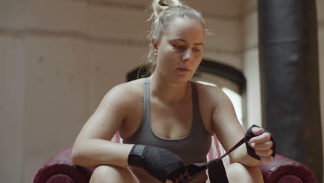 Medium-shot-of-focused-woman-rolling-bandage-on-hand-in-gym