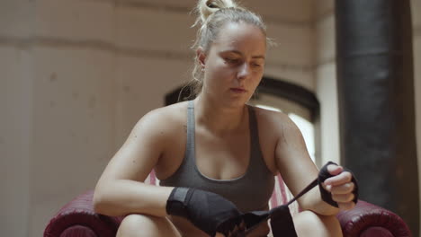 medium shot of focused woman rolling bandage on hand in gym