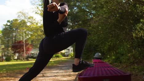 stretching on a park bench, this leggy brunette athlete warms up her muscles for a vigorous run at an isolated park