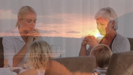 animation von sonnenuntergang über multigenerative kaukasische familie, die vor der mahlzeit zusammen betet