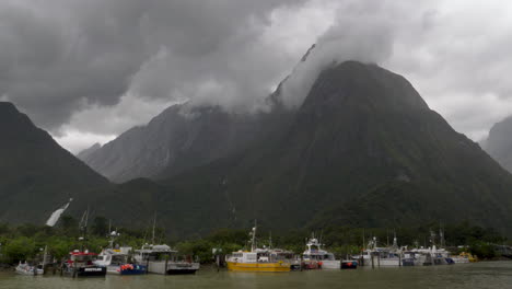 imágenes de 4k de una flota de barcos de pesca debajo de una montaña nublada en milford sound - piopiotahi, nueva zelanda