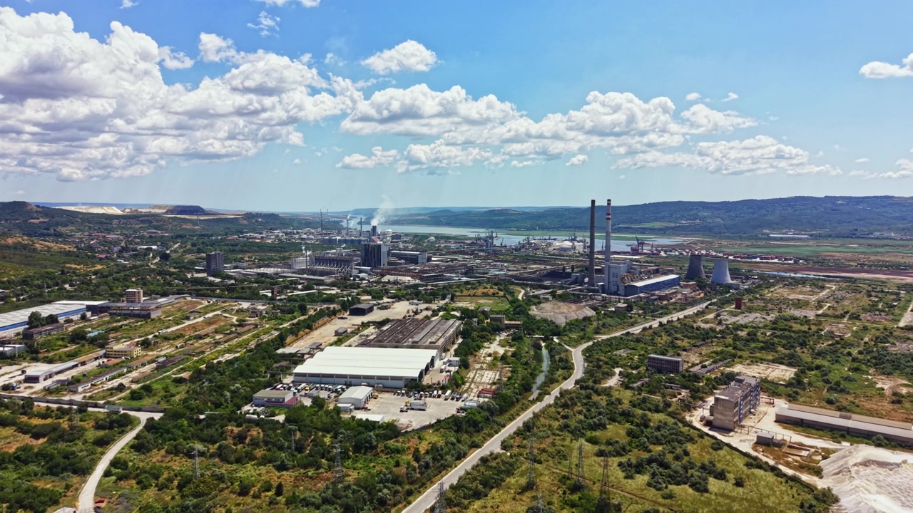 Vista de una zona industrial con fábricas, edificios y un río bajo un cielo azul con nubes, tomada desde arriba durante el día