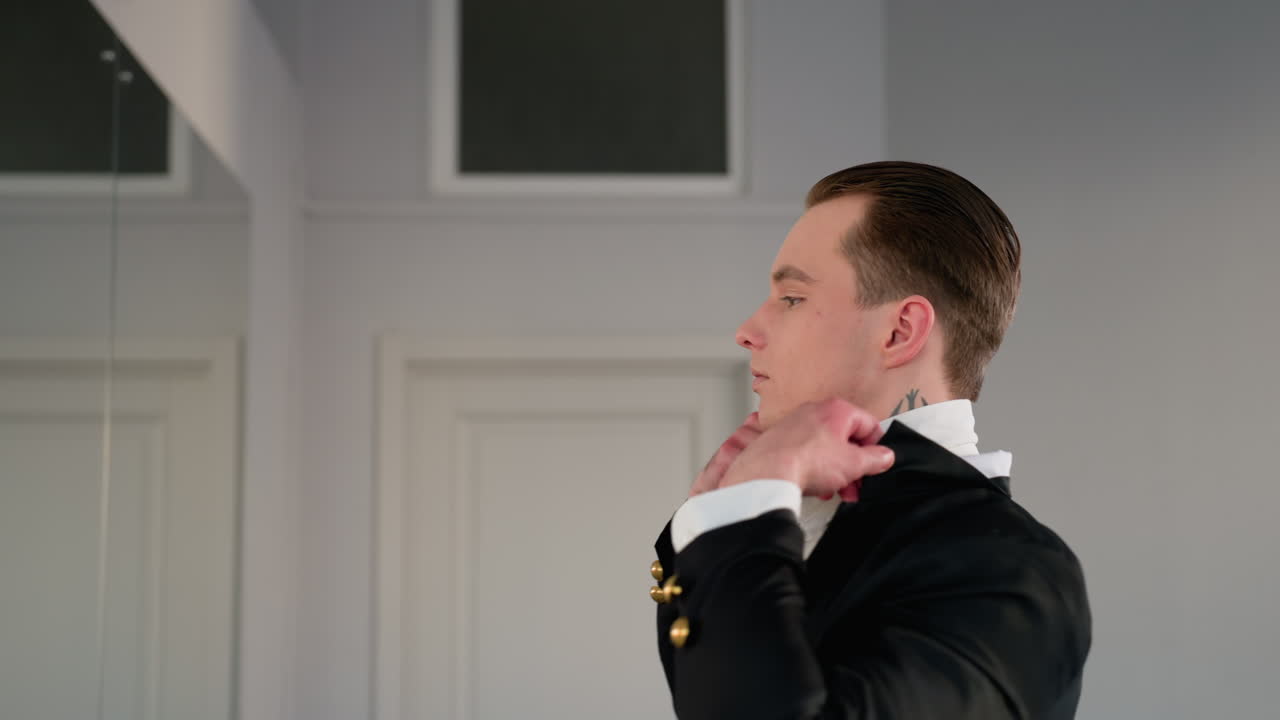 young lawyer adjusts collar in front of mirror before work, standing with arms raised in bright minimalist office setting, showcasing professional attire and confident morning routine