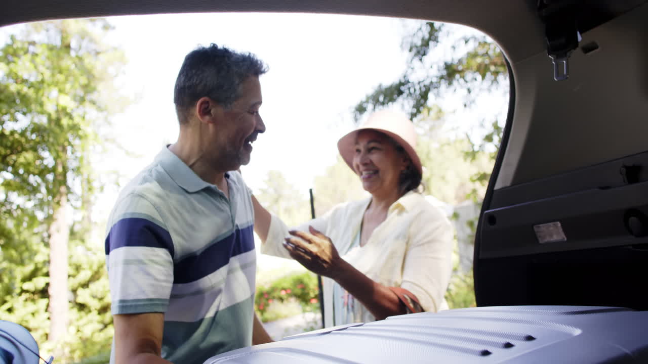 una feliz pareja de ancianos que empacan equipaje a un coche en un lugar soleado