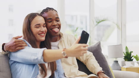 Tongue-out,-selfie-and-couple-kiss-in-home-on-sofa