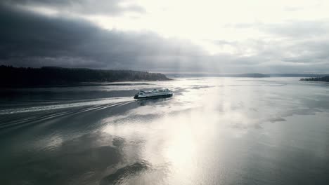 the brilliant morning sun streams through dark gloomy clouds as a ferry passes, aerial orbit