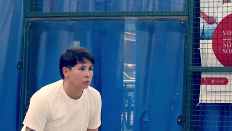 Young-woman-hitting-a-backhand-shot-with-racket-to-the-ball-in-indoor-padel-court