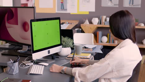 female graphic designer using digital drawing tablet and looking at monitor with green screen in an animation studio 1