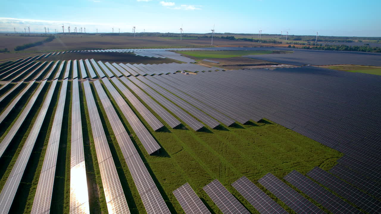 вид с воздуха на огромные панели солнечной фермы с ветряными турбинами на заднем плане