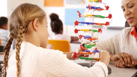 maestra ayudando a una escolar con un modelo de moléculas en el aula