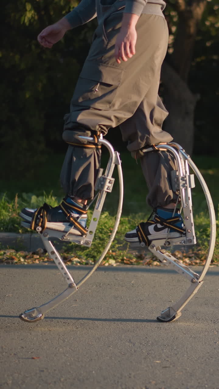 초록색 잔디와 나무로 둘러싸인 포장된 도로에서 회색 후디와 바지를 입고 기둥을 들고 는 남자, 역동적인 움직임, 균형, 야외 활동을 보여주고, 민함을 강조합니다.