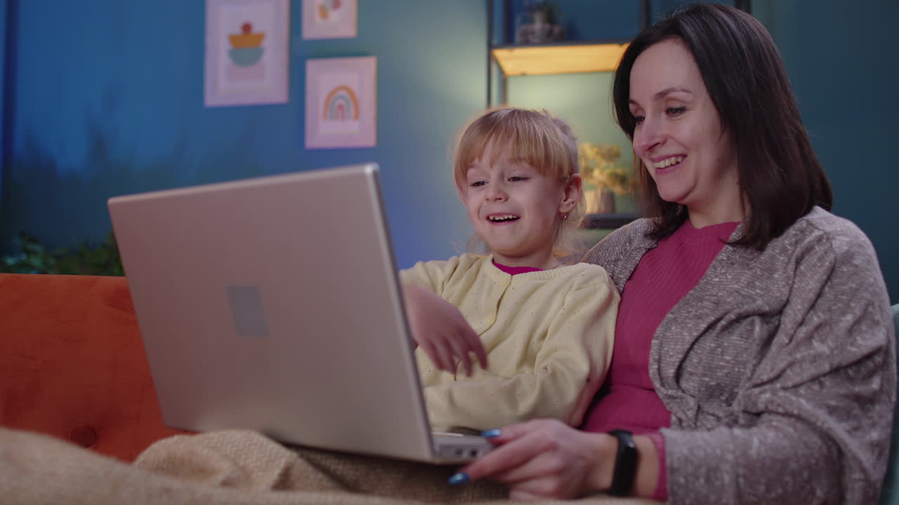 madre y niño pequeño hija niño estudio en la computadora portátil, viendo películas divertidas, relajándose, acostado en el sofá