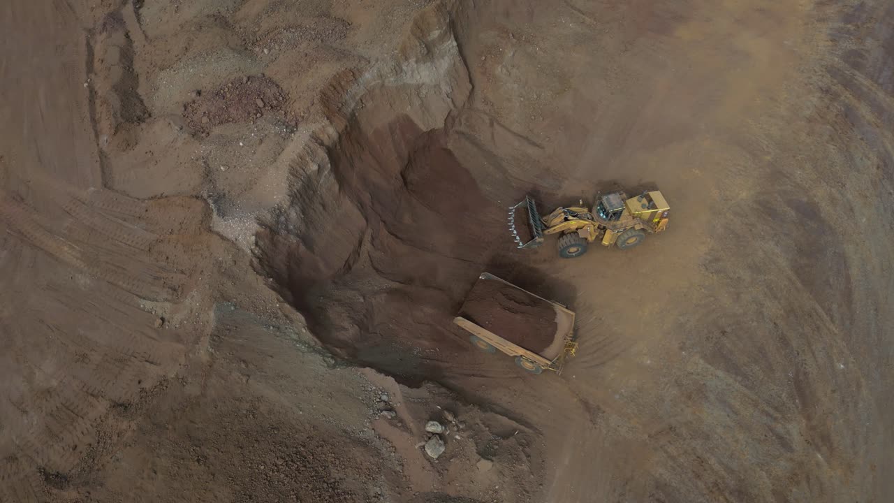 Excavator filling dump truck at nickel mine site, Western Australia, aerial top down shot
