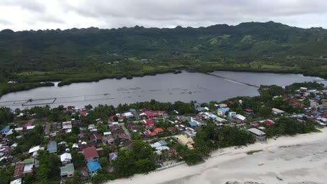 aerial drone fly above coastal city anda in philippines with houses and green tropical hills