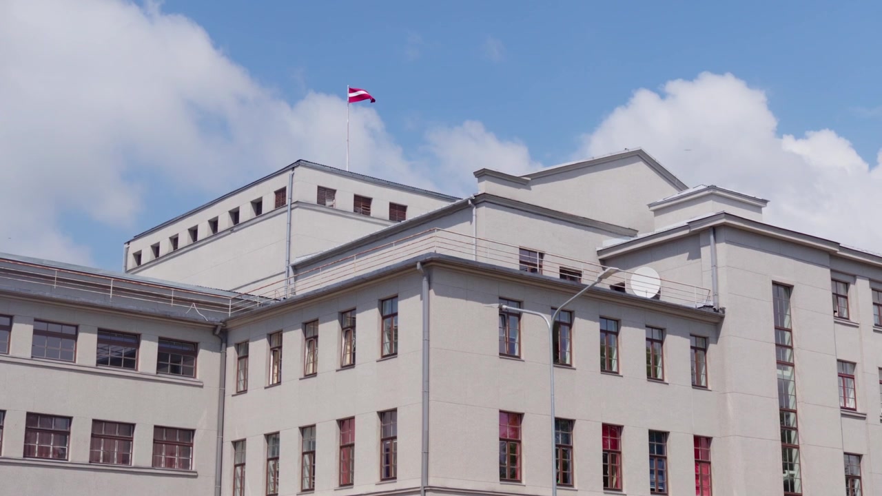 Tomada estática da fachada histórica do edifício Unity House com a bandeira nacional da Letônia tremulando no mastro sob o céu azul com nuvens na praça central de Daugavpils, Letônia