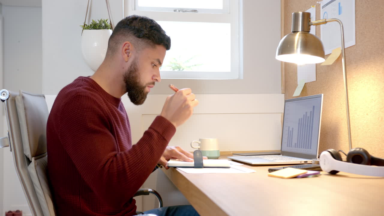 Working from home, man analyzing data on laptop and writing notes