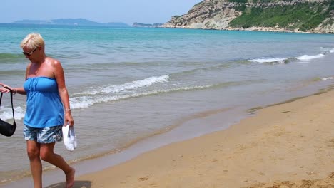 atractiva mujer de mediana edad caminando descalzo en la playa sintiéndose caliente durante el sol del mediodía corfú grecia