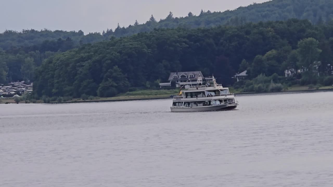 Perahu wisata di Danau Sorpe di wilayah Sauerland: Sebuah kapal penumpang putih berlayar di sepanjang pantai berhutan.