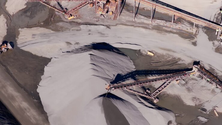 Top down aerial of conveyor belt casting shadow spreading over gravel pile as front loaders drive