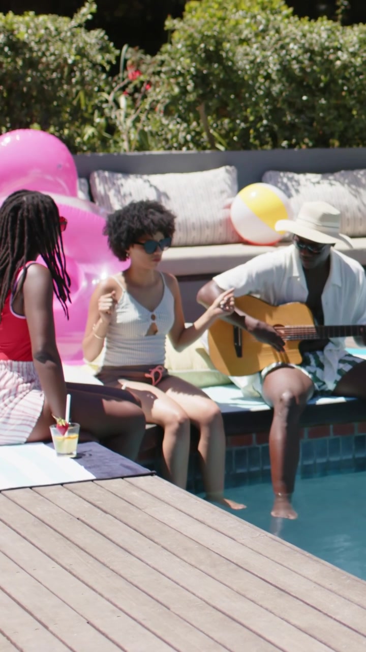Video verticale: Uomo con cappello che inizia a strimpellare la chitarra accompagnando amici che cantano in piscina.