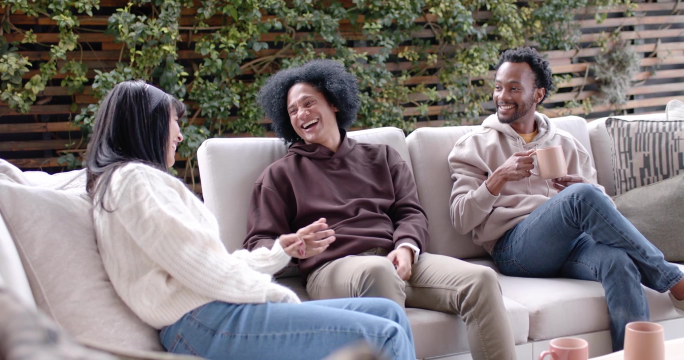African American friends on patio sofa, center speaker sharing story, right person sipping mug