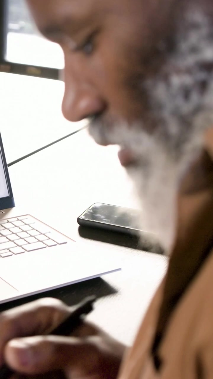 Vertical video: Leaning senior brown jacket seeing laptop screen using pen on tablet desk by window