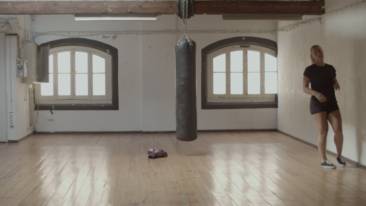 Long shot of young woman running with high knees in boxing room