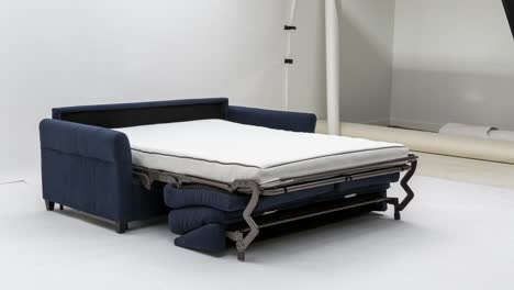 Camera-slowly-zooms-in-on-side-view-of-blue-pull-out-couch-bed-against-white-backdrop