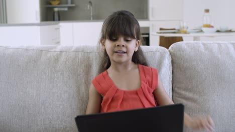 Cheerful-little-girl-sitting-on-couch-at-home