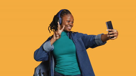 Girl-using-phone-to-take-selfies-doing-victory-hand-sign,-studio-background